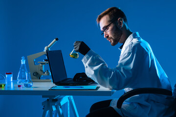 Poster - chemist sits sideways and enters the experiment data into the laptop. a man works in a chemical labo