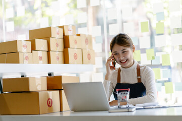 Young woman with mobile phone preparing parcels for shipment to client at home