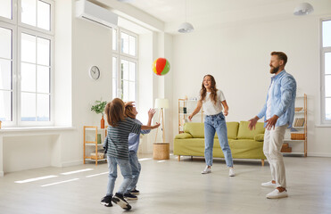 Happy family playing ball in the house. Cheerful young mother, father and little children playing football at home. Mommy, daddy and kids playing soccer with a toy ball and having lots of fun together