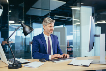 Wall Mural - Pensive boss working at computer in modern office, successful male businessman