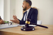 © Studio Romantic - Close up of judge's gavel on wooden table, with lawyer giving consultation in background, explaining controversial case, providing professional legal advice on problem in court. Law services concept