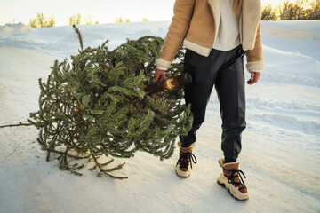 A woman drags an used Christmas tree to the dumpster. After Christmas. Snowy winter. Outdoors. Selective focus