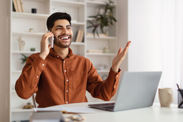 Wall Mural - Smiling Arab man working and talking on phone at home