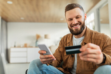 Poster - Happy Male Shopping Using Smartphone And Credit Card Sitting Indoors