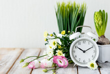 Spring Change, Daylight Saving Time Concept. White Alarm Clock And Flowers On The Wooden Table