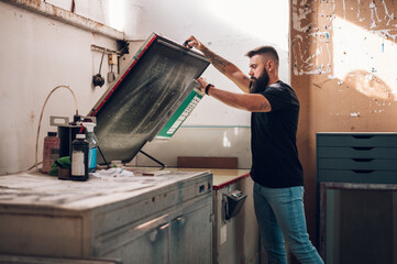 Wall Mural - Male worker using a screen exposure unit while working in a printing workshop