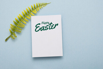 Wall Mural - Happy Easter Text on card with green leaf on blue paper background. Postcard easter lettering