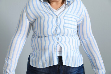 Wall Mural - Overweight woman in tight shirt on light grey background, closeup