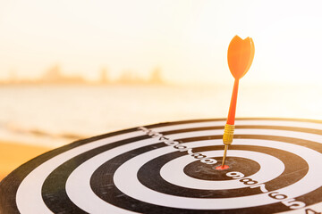 Dart arrow hitting to center on bullseye (bull's-eye) dartboard is the target of purpose challenge business at sunset, expert marketing strategy target, objective financial and goal success