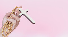 Rosary With Cross In Hand On Pink Background