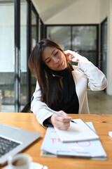 Wall Mural - Busy business woman talking on mobile phone and making note on notebook.