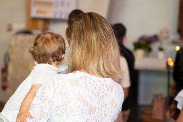 Baptism infant ceremony in Church in back view, blonde woman with child girl in white dress