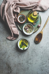 Healthy cooking ingredients on grey concrete kitchen table: olive oil, sage, garlic, pepper, salt, wooden cooking spoon, dish cloth. Cooking flavorful food at home. Top view.