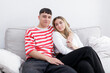© Maxim Morales - Happy embraced boy and girl sitting in the sofa smiling looking at camera. Young couple at home. Heterosexual 18-20 years old couple.