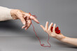 Hands of a young and an senior woman reach out to each other, connected by a red thread. Gray background. The concept of Alzheimer's disease.