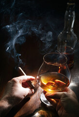 Male hands with glass of whiskey or brandy and smoking cigar