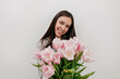 © PhotoBook - Wonderful happy woman with dark hair and lovely happy smile posing at camera with tender pink flowers over isolated background. Happy woman is celebrating Woman's Day