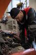 © pressmaster - Vertical portrait of male mechanic looking under hood while repairing car in auto shop