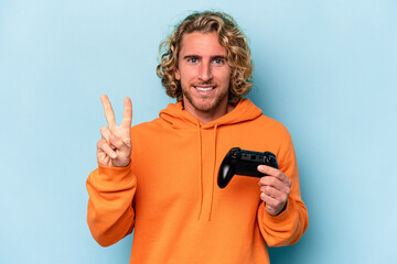 Wall Mural - Young caucasian man playing with a video game controller isolated on blue background showing number two with fingers.