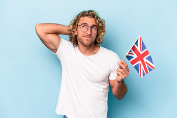 Wall Mural - Young student caucasian man holding an United Kingdom flag isolated on blue background touching back of head, thinking and making a choice.