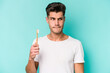 Young caucasian man brushing teeth isolated on white background confused, feels doubtful and unsure.