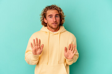 Wall Mural - Young caucasian man isolated on blue background rejecting someone showing a gesture of disgust.