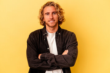 Wall Mural - Young caucasian man isolated on yellow background who feels confident, crossing arms with determination.