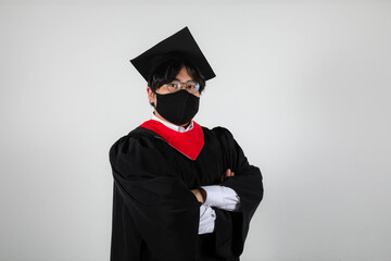 Wall Mural - Graduate in mask wearing a gown and a mortarboard hat on a white background