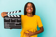 Young african american woman holding a clapperboard isolated on blue background  laughing and having fun.