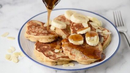 Wall Mural - Pouring maple syrup on vegan banana protein oat pancakes. Serving healthy breakfast. Closeup view white marble table