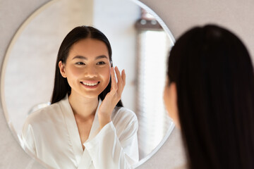 Wall Mural - Happy beautiful korean lady using moisturising face cream