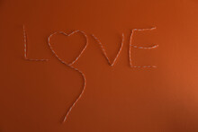 The Inscription "love" Decorative Rope. Isolated On Orange Wallpaper. 