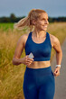 Happy athletic young woman enjoying an early morning run along a rural road as she looks to the side with a smile in a health and fitness concept