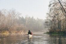 Two People In A Canoe Paddling On A Calm River, Misty Morning Scene