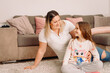 © Viorel - Happy woman in basic white t-shirt with her pretty lovely girl sitting on the carpet looking at each other with a smile.