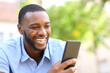 © PheelingsMedia - Happy man with black skin checking smart phone in a park