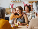 Fototapeta Panele - Cute little children embracing and kissing young happy mother while painting Easter eggs with family
