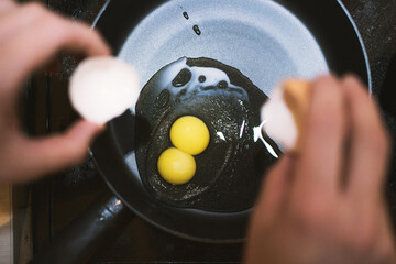 an egg with two yolks in a frying pan during the preparation of scrambled eggs. hands of a woman wit