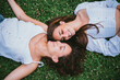 © Pablo Rasero - Two teenager girls smiling and looking at each other while they are laying down on grass in a park. They seem relaxed.