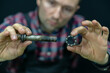 A bicycle mechanic holds damaged old bearings and a carriage shaft on a black background. Replacement of Bottom Brackets for bike. The guy's face on a black background with details in his hands.