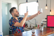 LGBT Man Taking Picture Of Rainbow Mug In The Kitchen During The Day. 