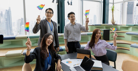 A group of construction engineers or real estate architectures from different genders and cultures with LGBT flags in their hands to support gender equity in a green office