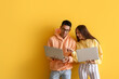 Young couple using laptops on yellow background