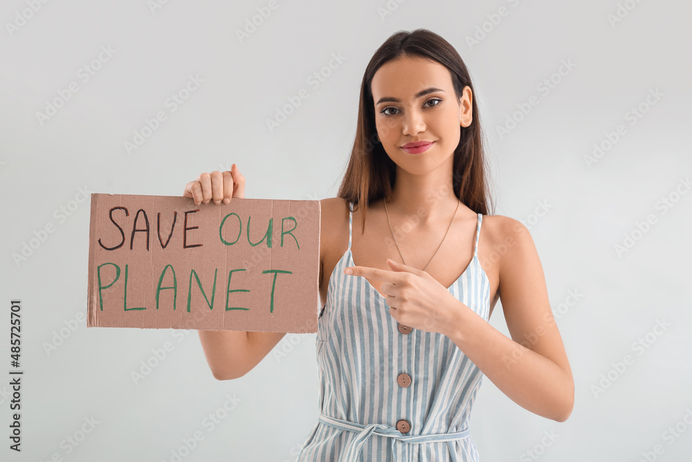 Young woman pointing at cardboard paper with text SAVE OUT PLANET on light background
