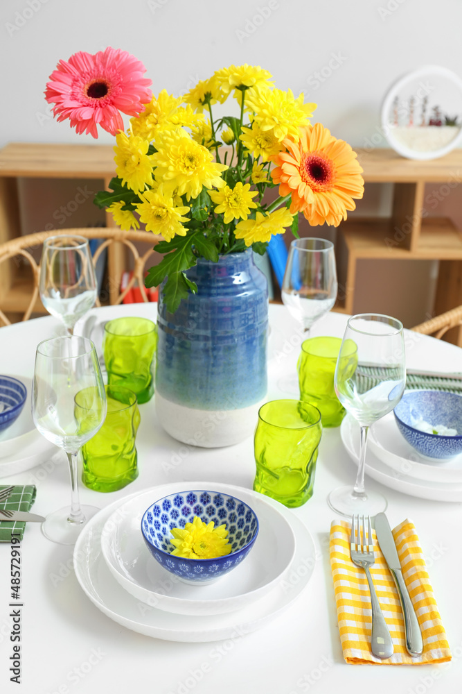 Dining table with stylish setting and beautiful flowers in room