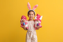 Funny Little Girl With Bunny Ears And Toys On Yellow Background. Easter Celebration