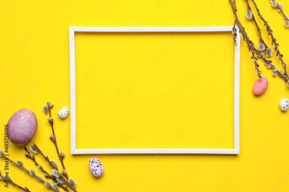 Easter composition with blank photo frame, willow branches and eggs on yellow background