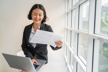 Fototapete - business woman smiling with holding paper and using laptop in office
