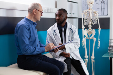 Senior old patient signing medical document during clinical appointment in hospital office. Specialist therapist doctor explaining sickness diagnosis discussing medication treatment