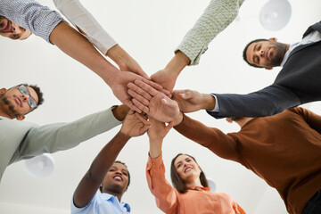 Diverse business team joining hands. Mixed race group of young people standing in circle and putting hands together, shot from below. Teamwork, help, support, success concept